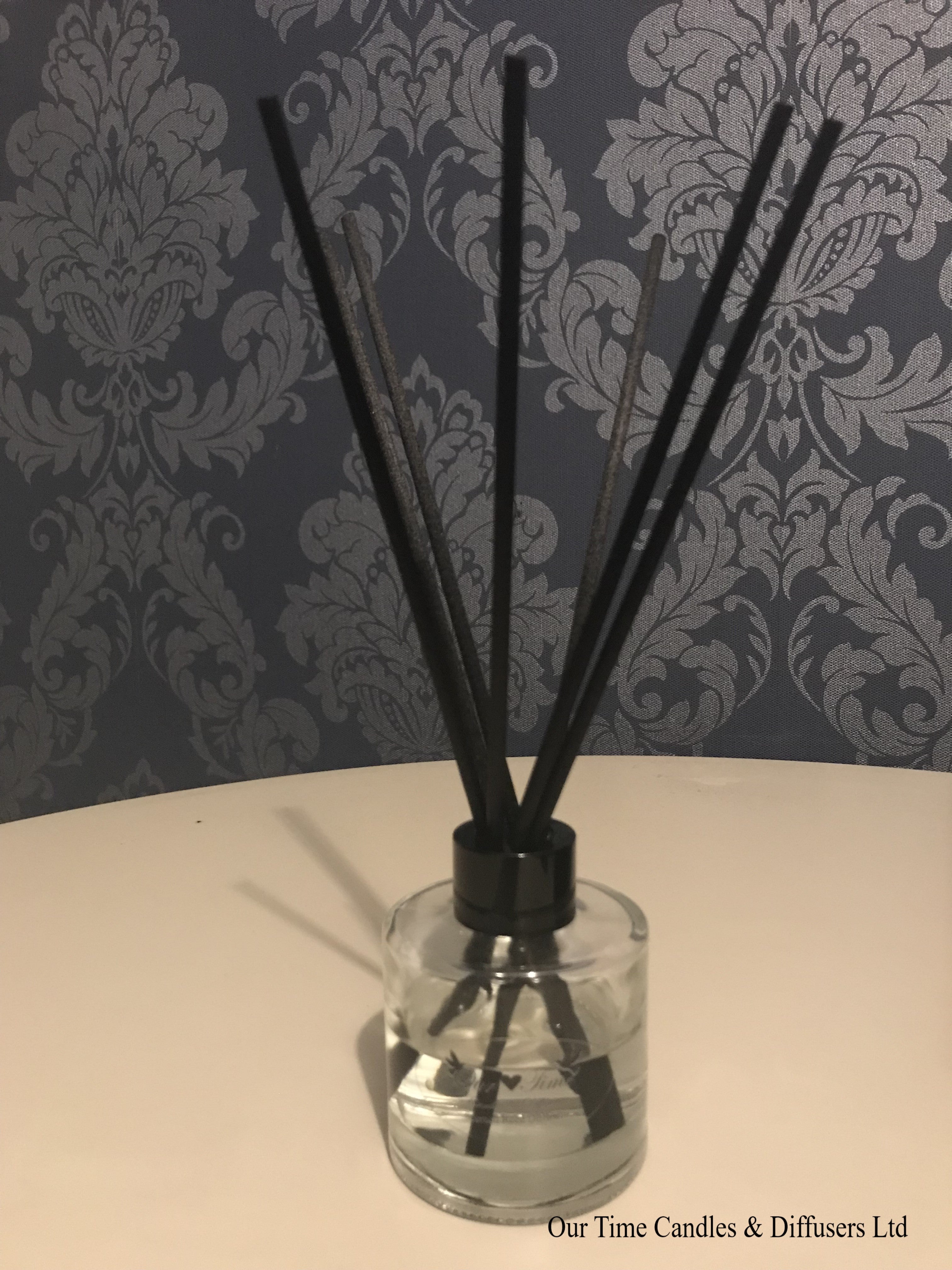 Clear reed diffuser with black cap and black reeds on an ivory table